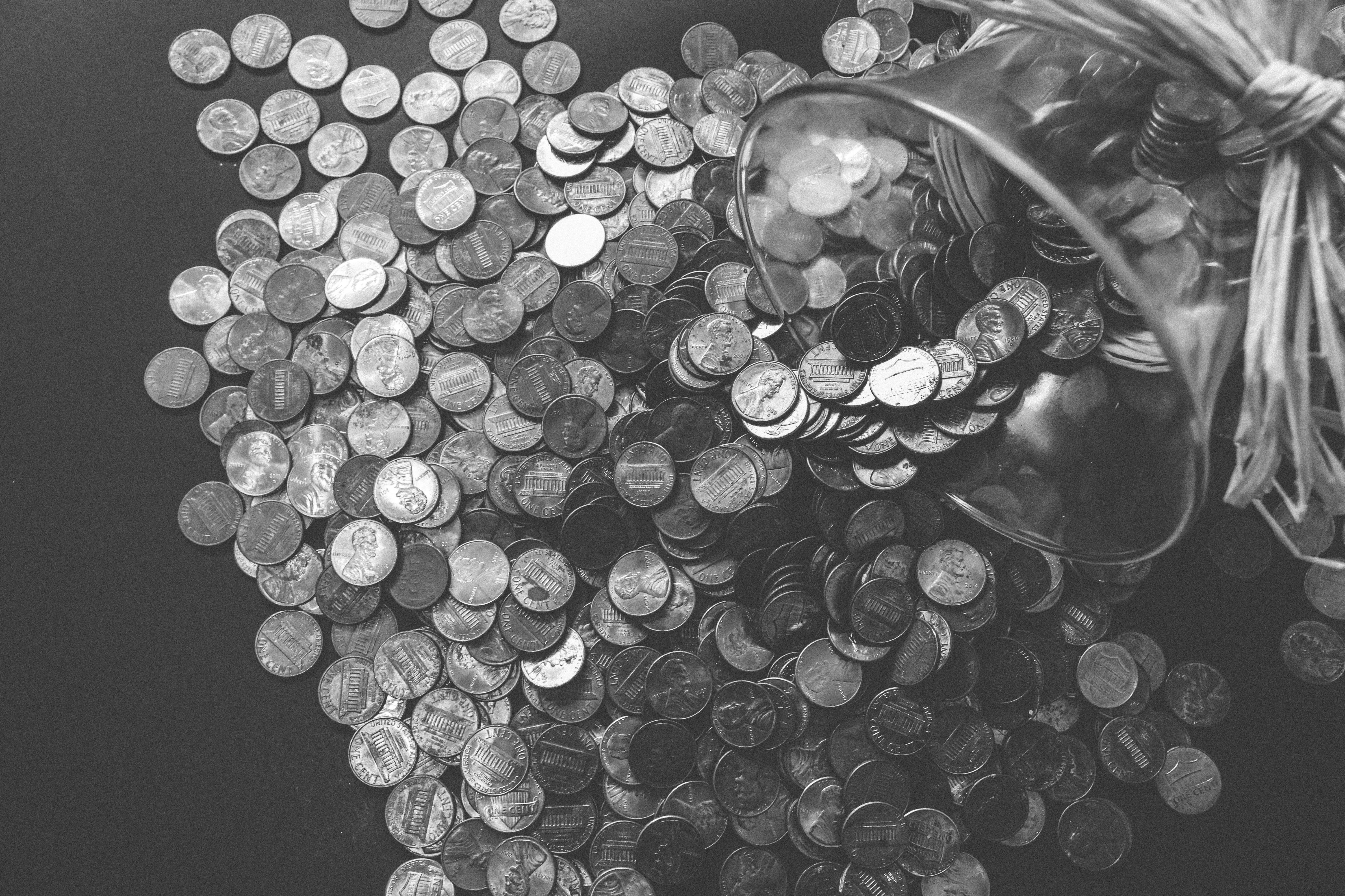 Grayscale photo of coins falling out of a jar