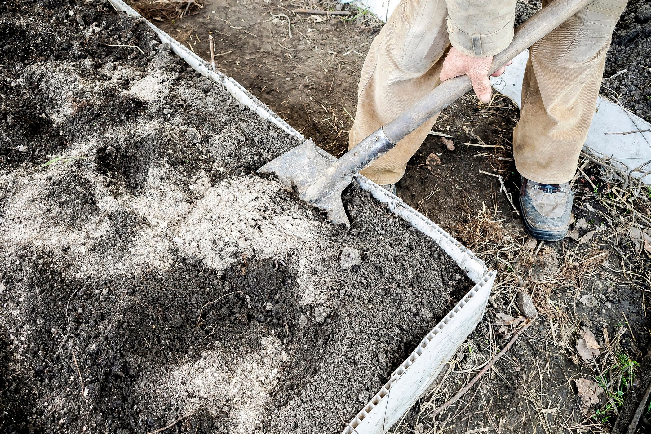 A gardener digging in a raised bed vegetable garden with shovel.