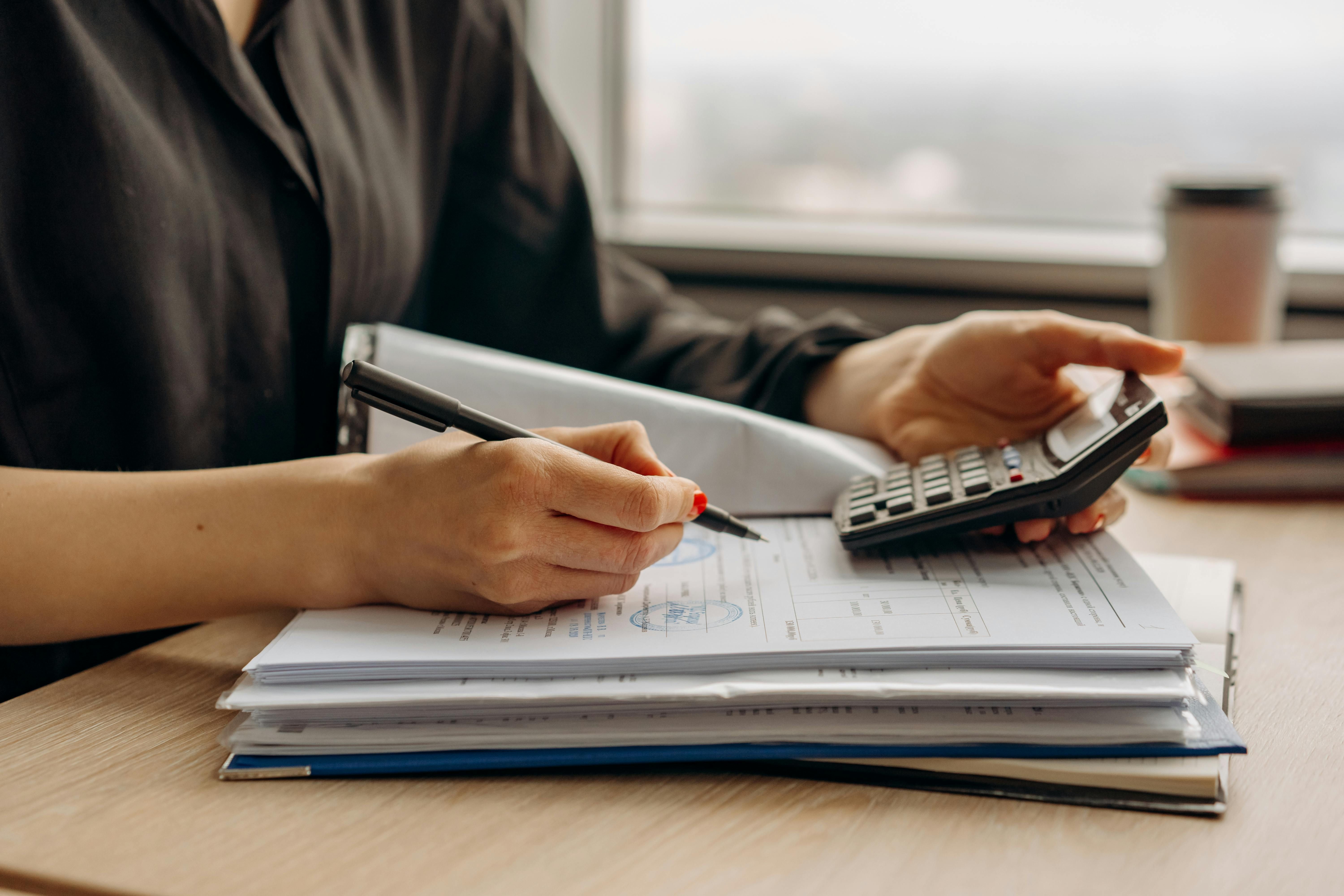 A person calculating using a calculator and writing the data to a paper using a pen.